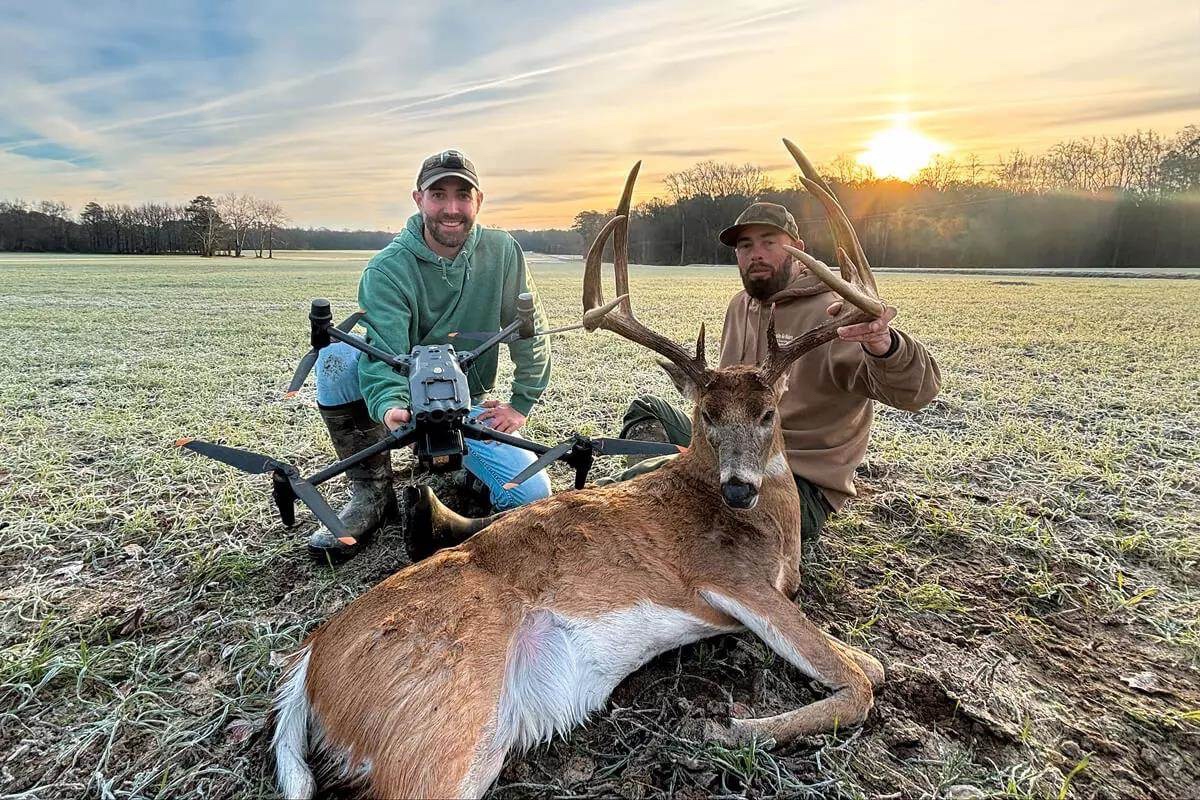 Jut Updyke kneeling with his DJI drone next to a recovered whitetail buck at sunrise